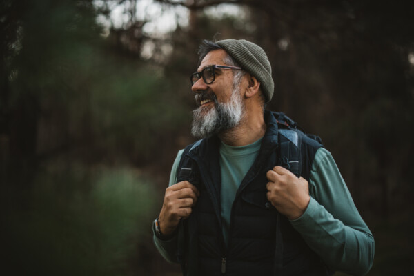 Portrait of mature man with backpack and camera hiking and taking photos in nature. Foto.